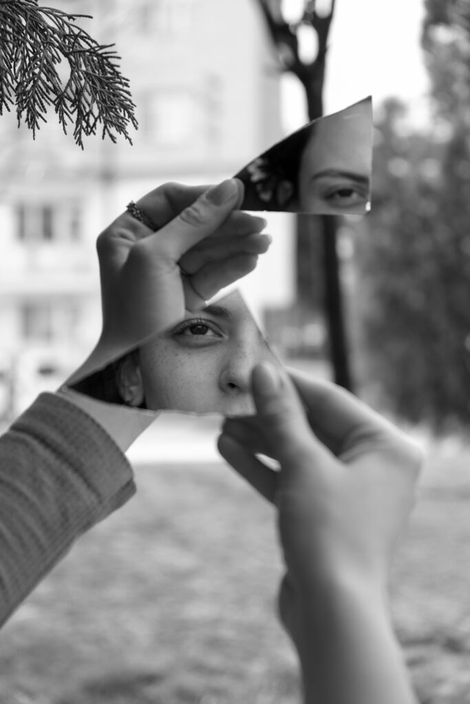 Black and white image of a woman's reflection in a broken mirror outdoors.