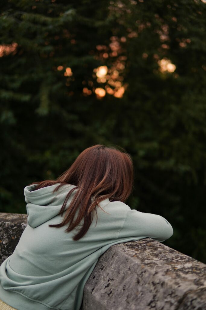Young woman leaning on stone ledge while enjoying sunset outdoors.