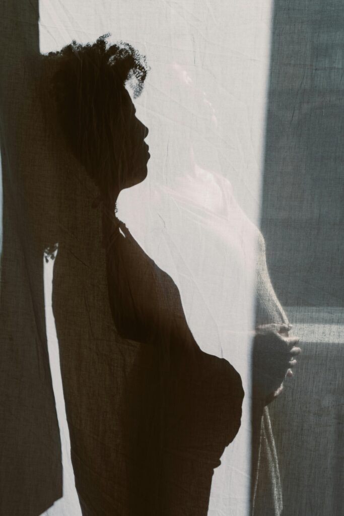 Artistic silhouette of a pregnant woman standing behind a curtain, highlighting her baby bump.