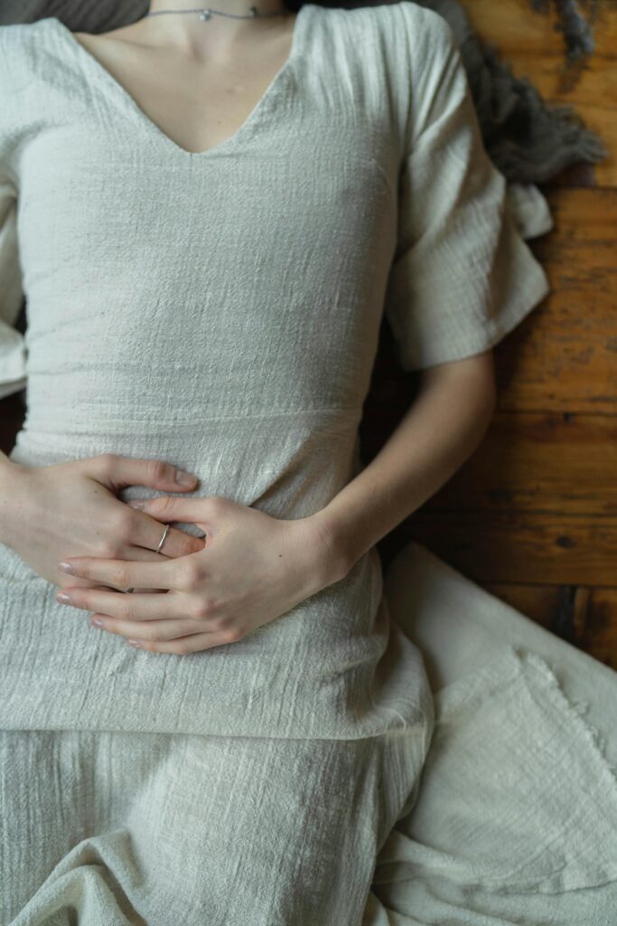 Close-up of a woman in a white dress lying down with hands gently resting together on a wooden floor.