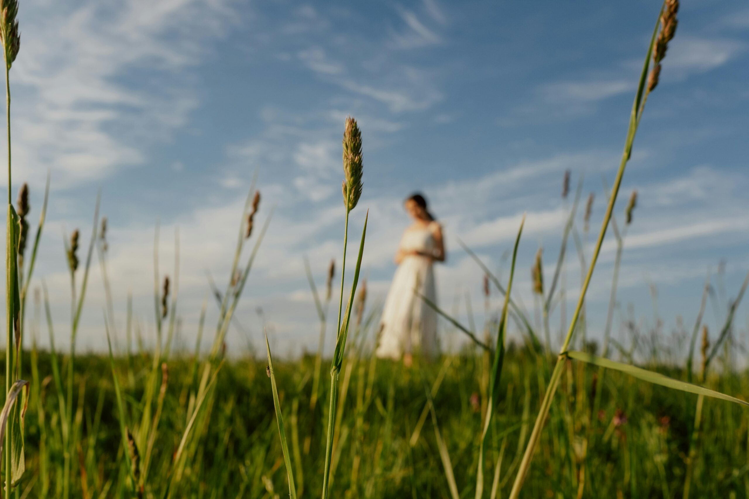 A woman in a white dress stands in a green field under a clear summer sky.