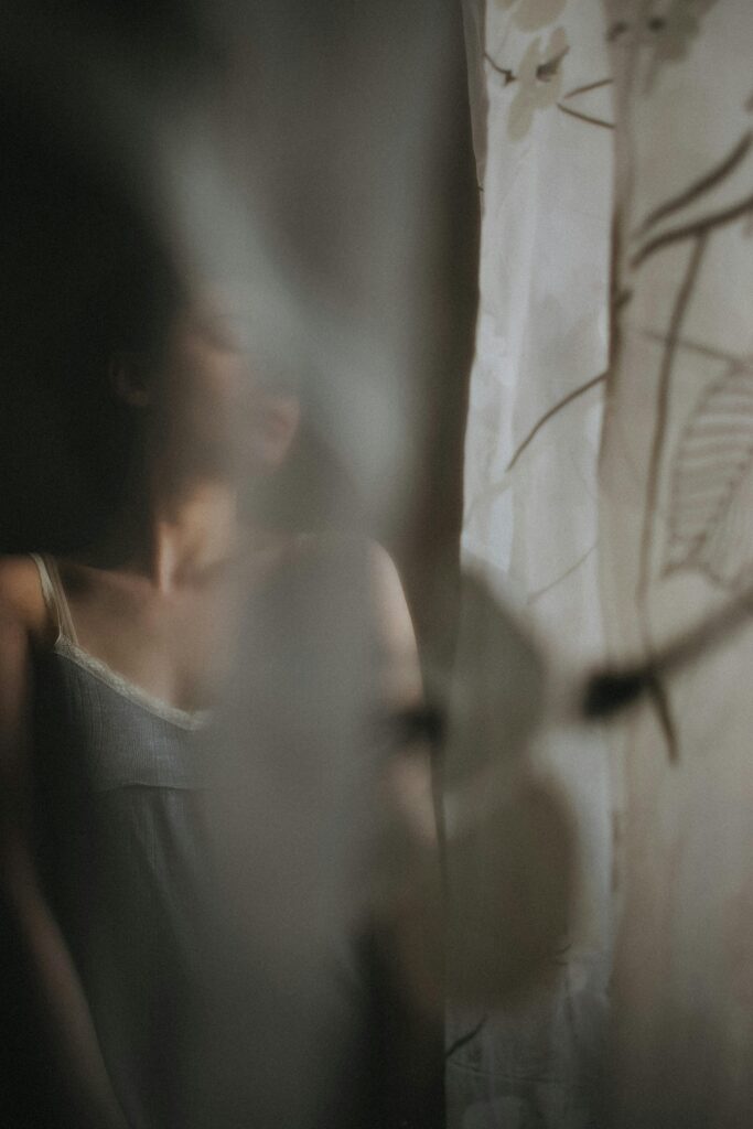 Artistic portrait of a woman obscured by a patterned lace curtain, creating a mysterious ambiance.