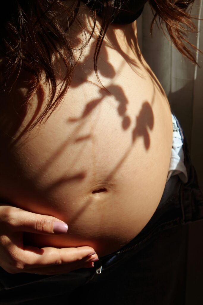 Pregnant woman's belly with artistic light and shadow play from nearby leaves.