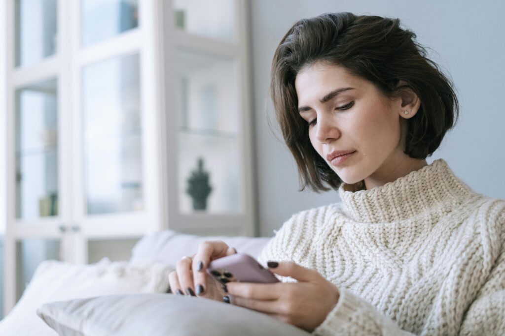 Woman in cozy knitted sweater using smartphone at home with a serene expression.